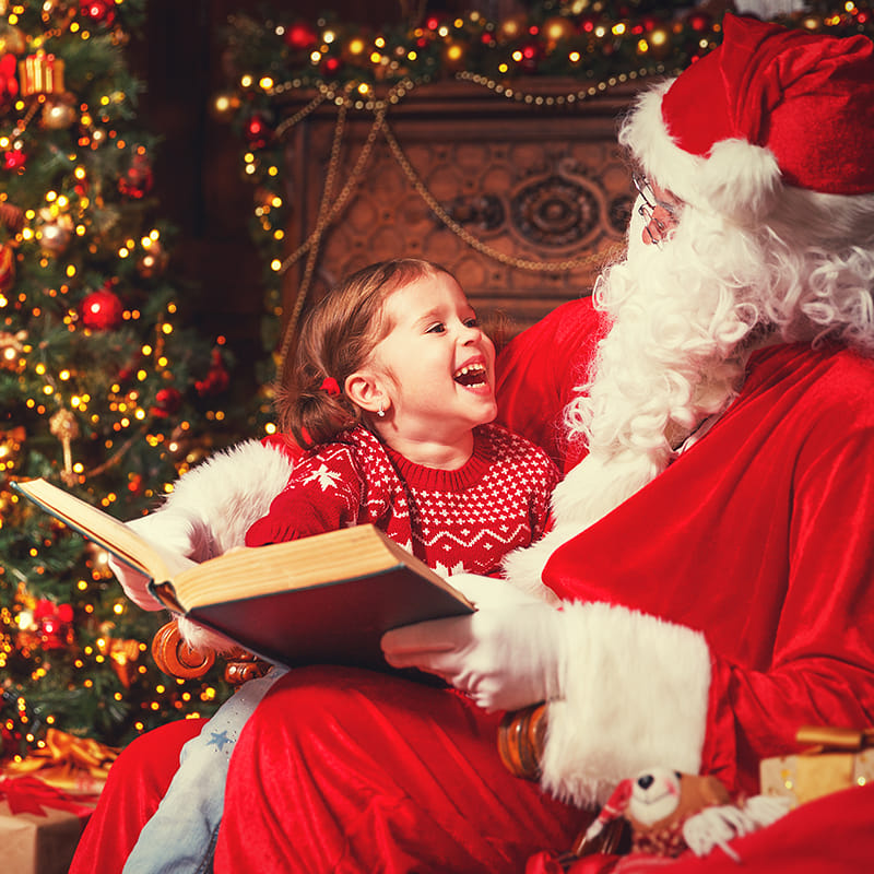 Niña leyendo un libro con papá Noel en Navidad